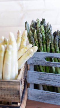 Tarafsız arka planda gri ve doğal ahşap bir sandıkta istiflenmiş kıtır yeşil ve beyaz kuşkonmaz mızrakları..