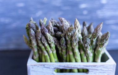 Gri arka planı tamamen taze ve bahar tarifleri için hazır olan zıt gri arkaplana karşı gri ahşap bir sandıkta gevrek yeşil kuşkonmaz yığını.