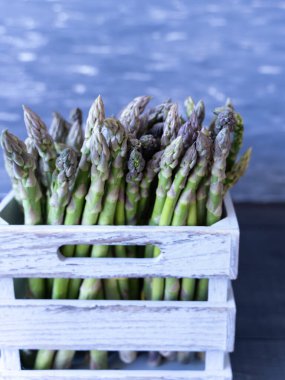Kırsal gri bir sandıkta canlı yeşil kuşkonmaz, doğal rengi ve mevsimsel tazeliği vurguluyor..