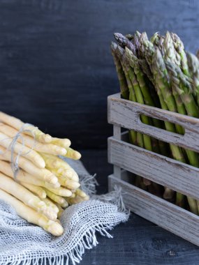 Tarafsız arka planda gri ve doğal ahşap bir sandıkta istiflenmiş kıtır yeşil ve beyaz kuşkonmaz mızrakları..