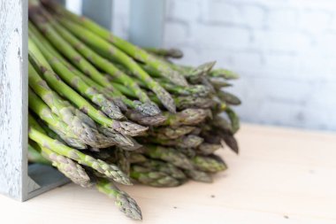 Tarafsız bir arkaplanda kırsal gri ahşap bir sandıktan düşen çıtır yeşil kuşkonmaz mızrakları.