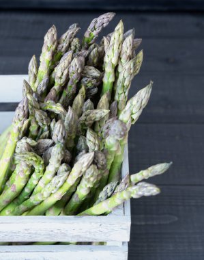 Gri ahşap bir sandığın içinde taze ve bahar tarifleri için hazır yeşil kuşkonmaz.