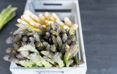 Kırsal gri bir sandıkta yeşil ve beyaz kuşkonmaz, doğal rengi ve mevsimsel tazeliği vurguluyor.