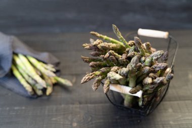 Taze yeşil kuşkonmaz kablo sepetinde, siyah ahşap yüzeyde mutfak bezine sarılı.