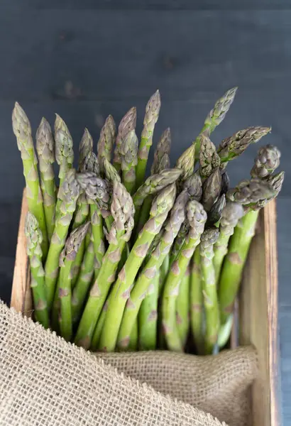 Tahta bir sandıkta, tepeden tırnağa yeşil kuşkonmaz, kısmen kırsal kumaşla sarılı.