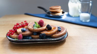 Böğürtlen ve muzla kaplı krep manzarası, süt şişesi ve arka planda mavi kumaş üzerinde ekstra yığın.