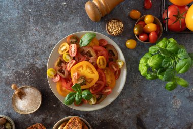Taze yaz salatasına hazır fesleğen, zeytin, tuz kasesi ve biber değirmeni ile dilimlenmiş domates manzarası.