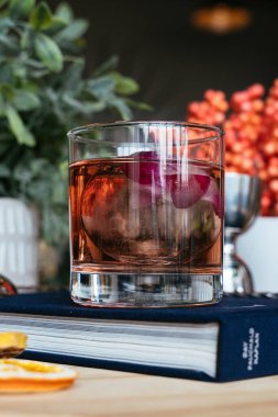 Hafif köpük ve çiçek tozuyla kaplanmış bir coupe bardağındaki pastel pembe kokteyl yumuşak ortam aydınlatmasında, doğal bir ahşap masa üzerine yerleştirilmiş..