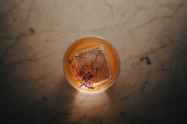 Safran ipliklerle kaplı kristal berraklığında servis edilen çağdaş bir kokteyl. Mermer ve ahşap yüzeylerde kaliteli cam kaplamalı karamsar ışıkta yakalanan, editoryal kullanım için mükemmel, lüks yaşam tarzı özellikleri, ya da karışımbilim odaklı kampanyalar.