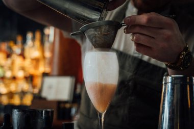 Kehribar rengi karışımı sıvılarla dolu süslü cam bitters kavanozu. Karmaşık oymalı tasarımlar içeriyor. Parlak bir ahşap çubuk yüzeyine kurulmuş bu resim, kalıtım karışımı ve zanaatkar içki sanatını vurgular..