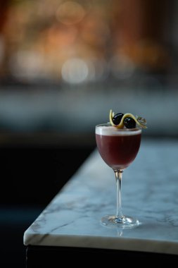 Derin kehribar negroni, kristal berrak bir buz küresinin üzerinde portakal kabuğuyla süslenmiş ağır bir bardakta servis edilir. Kalıplı ahşap bir yüzeye yerleştirilmiş, doğal ışık, mevsimsel promosyonlar veya bar menüleri için mükemmel, sıcak ve davetkar bir sahne yaratıyor..