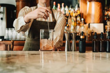 Barmen, uzun bir kaşıkla mermer barda kokteyli titizlikle karıştırıyor.