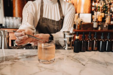 Barmen mermer barda viski kokteyli yapmak için cımbız kullanıyor. DM202504