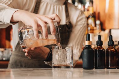 Barmen mermer barın üzerine taze buz küplerinin üzerine kokteyl döküyor. DM202504