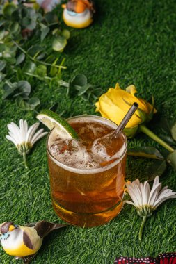 Misket limonuyla süslenmiş viski kokteyli, papatyalar arasında canlı bahar otları ve sarı bir gül üzerinde dinleniyor..