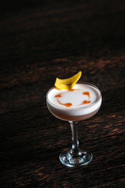 Limon kabuğuyla servis edilen parlak bir kokteyl köpüklü kalpleri acıtır, koyu renk ahşap zemin üstüne..