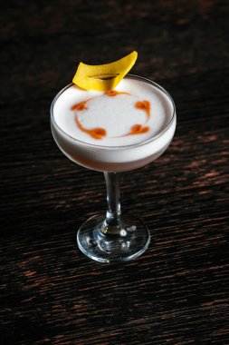 Kayalarda taze fesleğen yapraklarıyla süslenmiş, ahşap bir masada yuvarlak bir bardakta sergilenen parlak bir kokteyl..