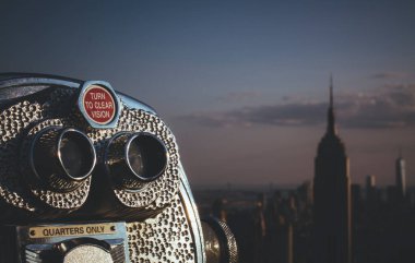 Günbatımında arka planda Empire State Binası ile New York şehrinin siluetine bakan madeni paralı dürbünler..