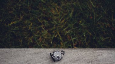 Kaliteli bir cep saati, zarif ve zamansızlığı vurgulayan yeşil çimen arka planlı ahşap bir yüzeye dayanır..