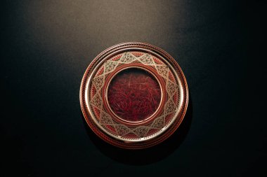 Safran iplikçiklerinin üst görüntüsü, karmaşık bir şekilde tasarlanmış, koyu arkaplanda metal bir kapta..