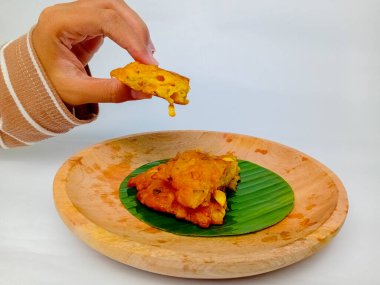 Bir parça Dadar Jagung ya da Endonezya mısır böreği tutuyorum. Tahta bir tabakta, yuvarlak bir muz yaprağında servis edilmiş, beyaz arka planda izole edilmiş..