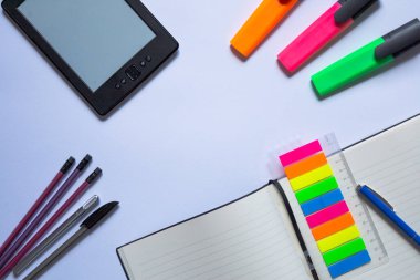 Not Defteri ve Vurgulayıcıları olan Düzenli Çalışma Alanı. Dijital okuyucu, renkli fosforlu kalemler, kalemler ve yapışkan notlar ve cetvelli açık bir defterin yer aldığı düzenli bir çalışma alanı. Ofis, eğitim ve üretkenlik temaları için ideal