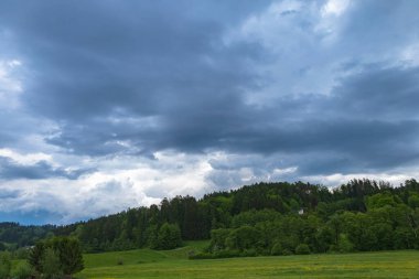 Yeşiller Üzerinde Dramatik Gökyüzü. Yoğun ormanlık tepelerle dolu yemyeşil bir arazide yuvarlanan kara fırtına bulutlarının büyüleyici bir görüntüsü dramatik ve karamsar bir atmosfer yaratıyor..