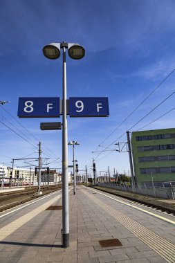 8F ve 9F 'yi gösteren işaretleri olan terk edilmiş bir tren istasyonu. Açık mavi gökyüzü ve çevreleyen şehir binaları huzurlu ve modern bir atmosfer yaratıyor.