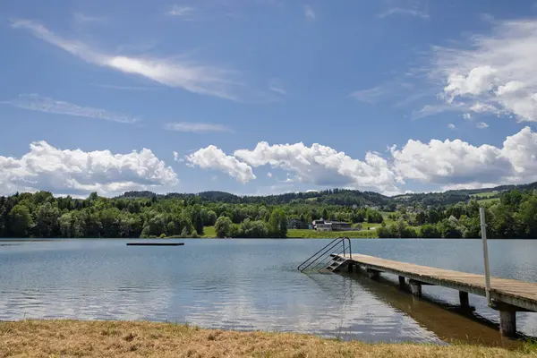 Pier ve kırsal bölge manzaralı Lakeside Manzarası. Ahşap bir iskele, yemyeşil yemyeşil ve uzak bir kırsal bölgenin yer aldığı sakin bir göl manzarası..