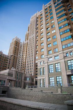 Gotik mimari elementlere sahip, yüksek kuleleri ve taş cepheleri olan, berrak mavi gökyüzüne karşı kurulmuş, kentsel karmaşıklığı gözler önüne seren modern yüksek binalardan oluşan bir küme.