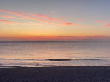 Gün doğumunda Santorini 'de yumuşak bir deniz, siyah kum ve bir kuş uçuyor. Yüksek kaliteli FullHD görüntüler