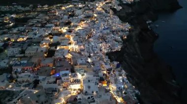 Oia, Santorini, Beyaz Yıkanmış Kubbeler ve Altın Sokak Işıkları üzerindeki hava alacakaranlığı. Yüksek kalite 4k görüntü