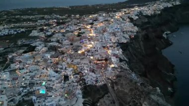 Oia, Santorini, Beyaz Yıkanmış Kubbeler ve Altın Sokak Işıkları üzerindeki hava alacakaranlığı. Yüksek kalite 4k görüntü