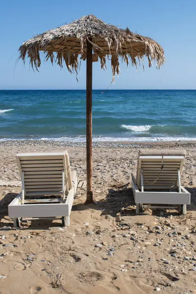 Geleneksel Girit şemsiyeli yaz havası ve sahilde iki güneşli yatak. Yüksek kalite fotoğraf