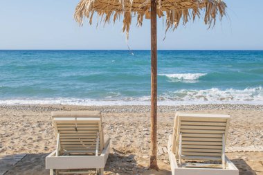 Çakıl taşlı bir sahilde basit Girit sahnesi, kır şemsiyeleri ve güneşli yataklar. Lüks yok, aşırılık yok. Sadece güzelliğin sadelik ve denizin sesi içinde yaşadığı yerel hayatın zahmetsiz cazibesi. Yüksek kalite fotoğraf