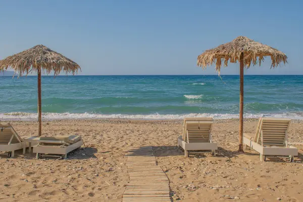 Çakıl taşlı bir sahilde basit Girit sahnesi, kır şemsiyeleri ve güneşli yataklar. Lüks yok, aşırılık yok. Sadece güzelliğin sadelik ve denizin sesi içinde yaşadığı yerel hayatın zahmetsiz cazibesi. Yüksek kalite fotoğraf