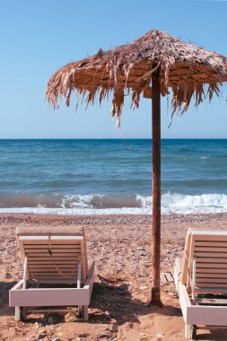 Girit 'te basit bir plaj sahnesi. Güneş yatakları ve çakıl taşları ve deniz kenarında palmiye yaprağı şemsiyeleri. Yüksek kalite fotoğraf