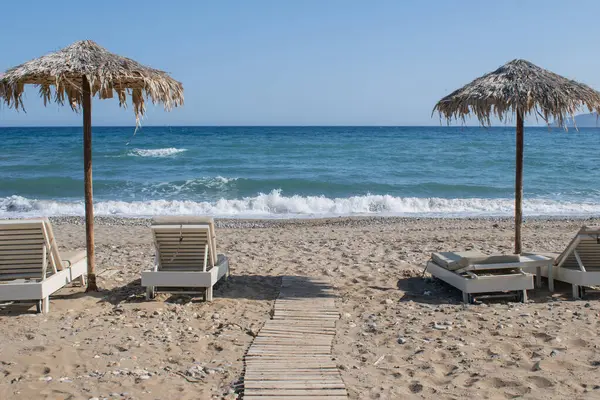 Girit 'te basit bir plaj sahnesi. Güneş yatakları ve çakıl taşları ve deniz kenarında palmiye yaprağı şemsiyeleri. Yüksek kalite fotoğraf