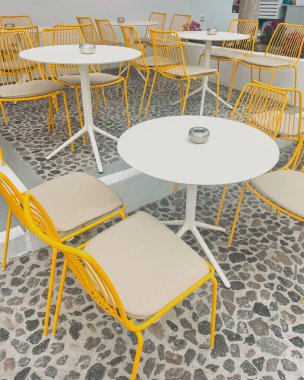 Sarı metal sandalyeleri ve beyaz yuvarlak masaları olan alışılmadık Santorini tarzı rahat bir kafe. Yüksek kalite fotoğraf