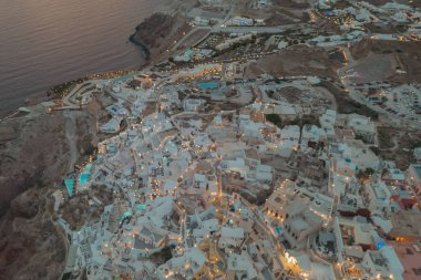 Oia, Santorini, Yunanistan. Beyaz sarayları aydınlatan sıcak sokak ışıklarıyla akşam hava aracı manzarası. Yüksek kalite fotoğraf