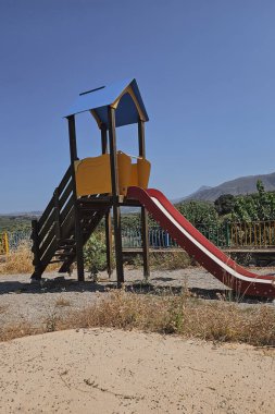 Oyun parkında dağ manzaralı ve zeytinlikleri olan bir ev şeklinde renkli bir kaydırak. Yüksek kalite fotoğraf