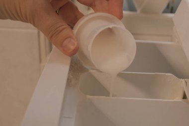 Kadın eli kapaktan çamaşır makinesinin deterjan bölmesine kumaş yumuşatıcısı döküyor. Yüksek kalite fotoğraf