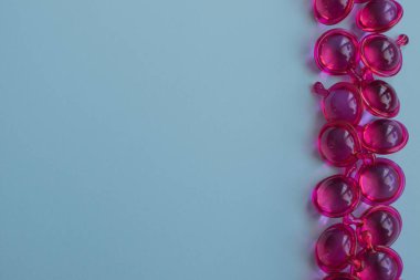 Açık mavi zemin üzerinde pembe tüylü vitamin kapsülleri ve fotokopi alanı. Yüksek kalite fotoğraf