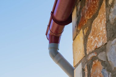 Taştan bir duvarın yakınındaki yağmur suyu drenaj sistemi çatıdan yağış toplamak ve yönlendirmek için tasarlanmış. Yüksek kalite fotoğraf