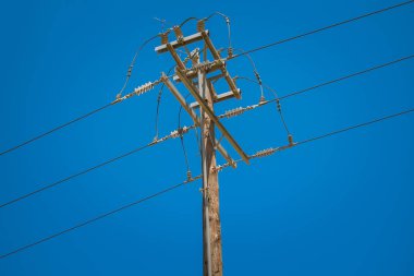 Yerin üstünde açık mavi gökyüzüne karşı elektrik iletimi için kablolar olan elektrik direği. Yüksek kalite fotoğraf