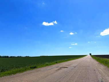 Bereketli otlaklar ve parlak mavi gökyüzü arasındaki mesafeye giden uzun bir yol. Seyahat, macera ya da doğa temaları için mükemmel bir görüntü.
