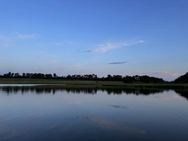 Sakin bir göletin üzerindeki bulutlu gökyüzünün akşam yansımaları sakin ve huzurlu bir doğal manzara yaratıyor..