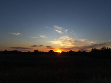 Altın gün batımı yoğun yaprakların arasından, renkli bulutların arasından ve kırsal kesimdeki sakin atmosferden süzülüyor.