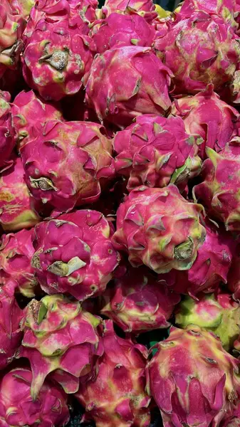 Geniş, canlı, pembe bir ejderha meyvesi yığını, eşsiz pullu derilerini ve renkli görünümlerini bir pazar ortamında sergiliyorlar..