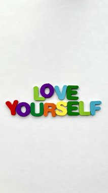 Beyaz arka planda renkli 'Kendini Sev' tahta harfleri.